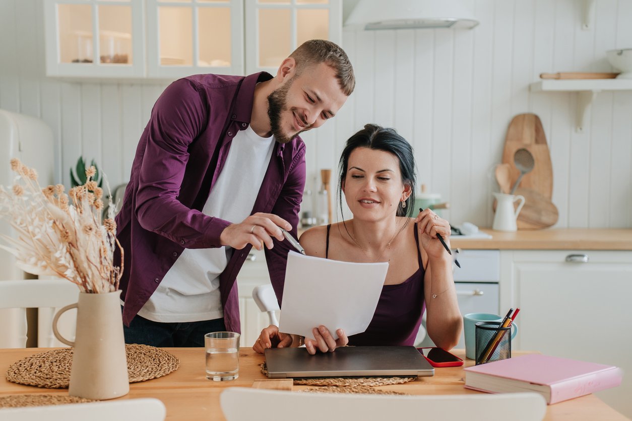 Bearded young man showing bills to wife sitting at desk at kitchen planning family budget at home.Young couple reading loan documents. 